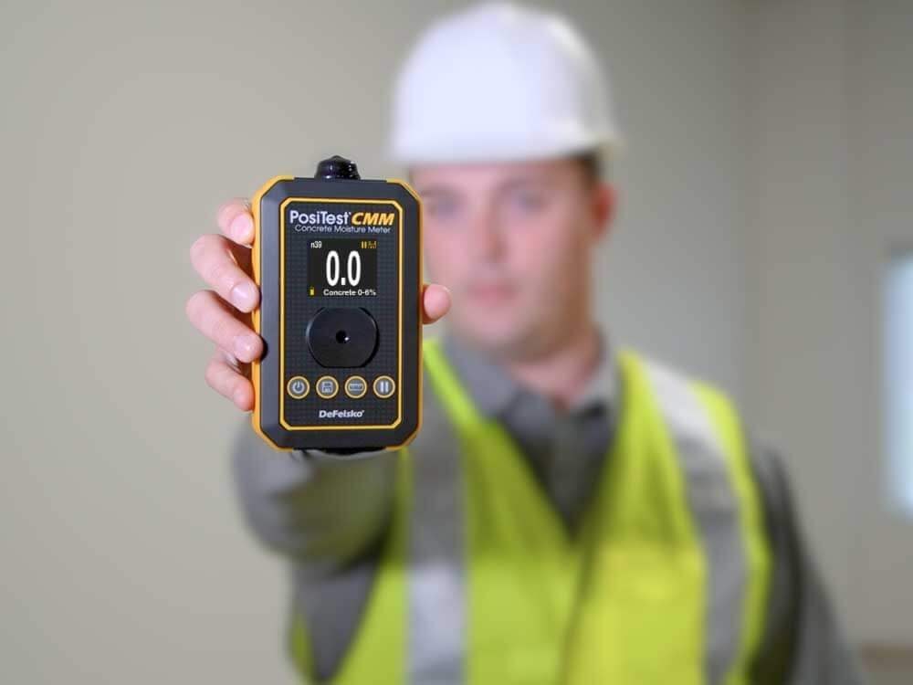 PosiTest CMM concrete moisture meter held by an inspector wearing a yellow construction vest